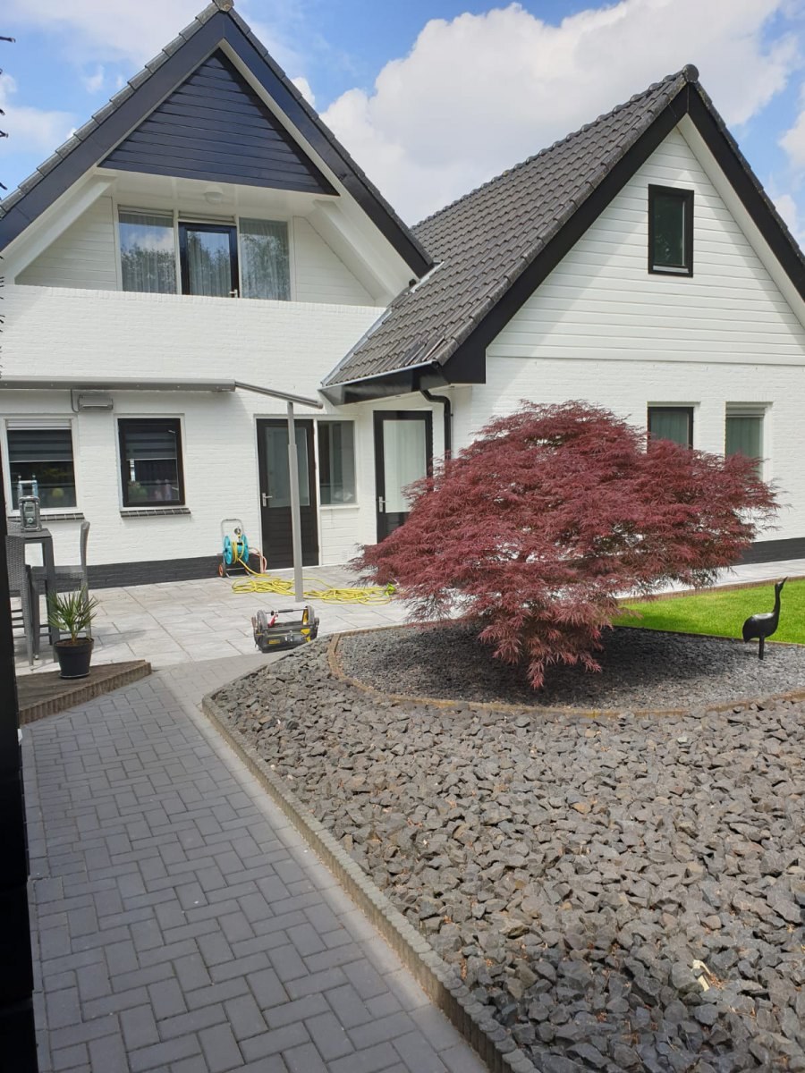 Wit afgewerkte woning met een rode esdoorn in de tuin